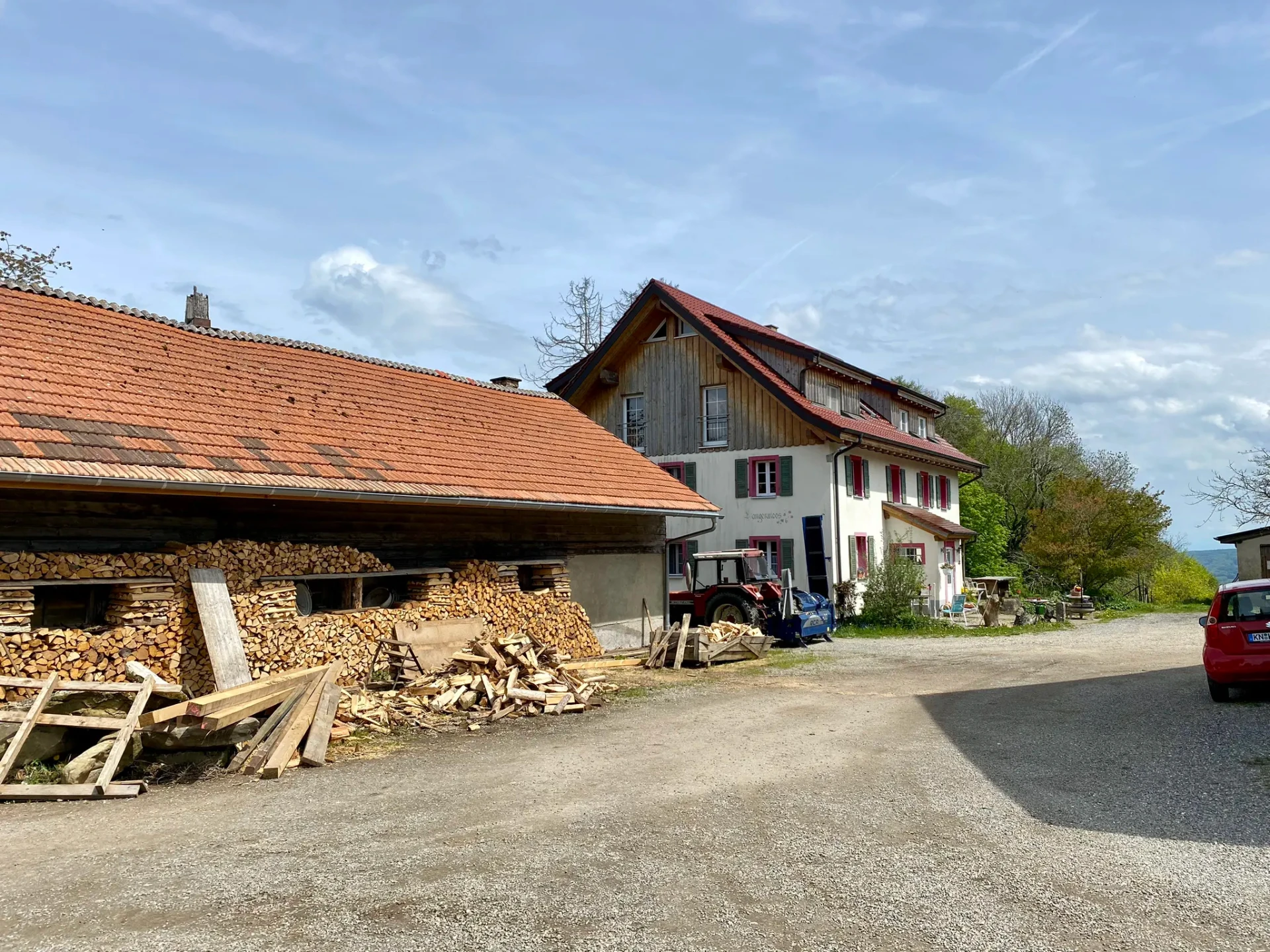 Hof Langenmoos: Wohnhaus mit Holzstapel und Traktor im Hof